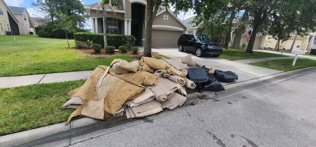 A pile of discarded carpet rolls and bags of waste awaits Pinellas Park Junk Removal collection on the curb of a residential street.